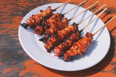 Tavuk satay ya da tavuk derisi satay beyaz tabakta kırmızı baharat ile ahşap masalarda izole