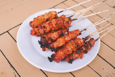 Tavuk satay ya da tavuk derisi satay beyaz tabakta kırmızı baharat ile ahşap masalarda izole