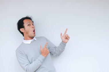 Genç Asyalı erkek waer beyaz gömlek şaşırdı ve haykırıyor sağ işaret ile sağ arka planda izole parmak ile metin boşluk.