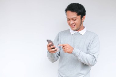 Zeki Asyalı genç adam stüdyo arka planında akıllı telefon kullanırken mutlu ve gülümsüyor.