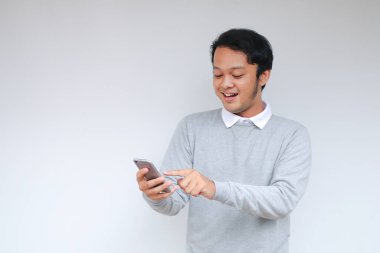 Genç Asyalı adam, gri arka planda gördüğü şey karşısında şok olmuş ve mutlu..