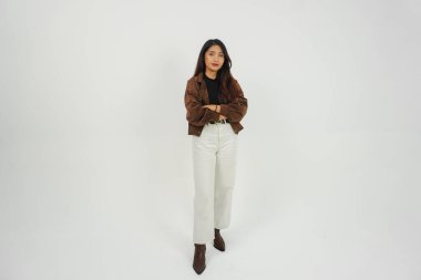 Kendine güveni tam bir genç kadın portresi. Sıradan kıyafetler giymiş, kollarını kavuşturmuş, izole beyaz arka planda poz veriyor.