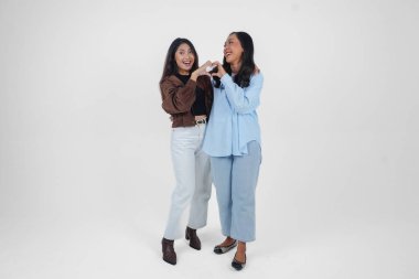 İki genç Asyalı kadın duygularını ifade ediyor, kalp hareketlerini şekillendiriyor, aşkını ifade ediyor, beyaz arka planla izole edilmiş. Arkadaşlık kavramı.