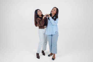 İki genç Asyalı kadın duygularını ifade ediyor, kalp hareketlerini şekillendiriyor, aşkını ifade ediyor, beyaz arka planla izole edilmiş. Arkadaşlık kavramı.