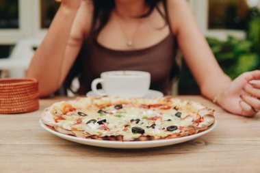 Pizza with olives, peppers, and cheese on top of a table in restaurant.
