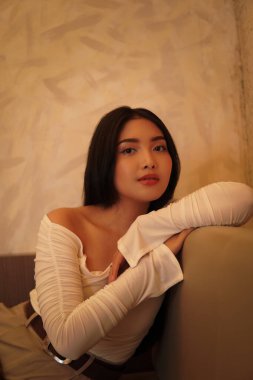 Pretty young Asian woman wearing white shirt is leaning on the couch posing at a restaurant.