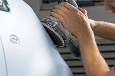 Araba tamirhanesinde araba cilalayan bir adamın elinde öğütücü..