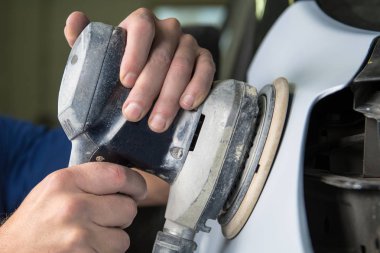 Araba tamirhanesinde araba cilalayan bir adamın elinde öğütücü..