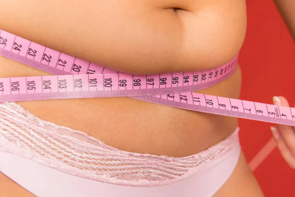 A fat woman measures the perimeter of a belly meter.
