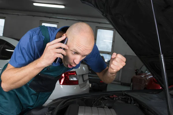 Young car service technician calling while repair the car engine motor.