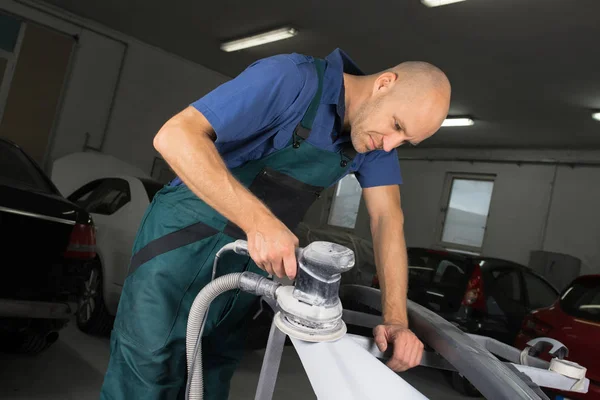 Grinder in the hands of a man who sharpen a car varnish in the car shop.