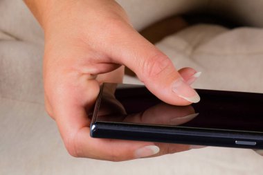 Kadın yatakta oturuyor ve cep telefonundan mesaj yazma.