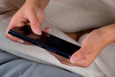 Kadın yatakta oturuyor ve cep telefonundan mesaj yazma.