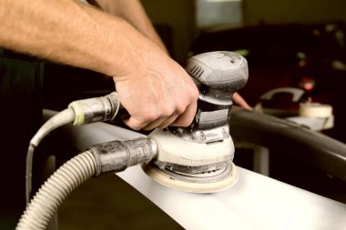 Araba tamirhanesinde araba cilalayan bir adamın elinde öğütücü..