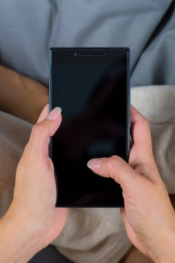 Kadın yatakta oturuyor ve cep telefonundan mesaj yazma.