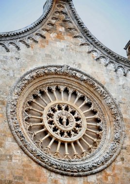 Ostuni Katedrali'nin ana girişi üzerindeki yuvarlak soketin geleneksel rozeti ve gotik mimarisi İsa Mesih'in cennet krallığını sembolize eder..