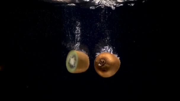 Filmación de kiwi cayendo en el agua sobre fondo negro — Vídeos de Stock