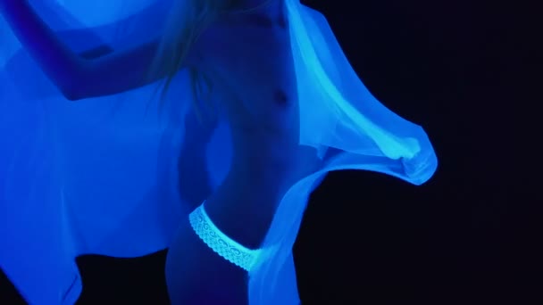 Çıplak göğüslü ve ultraviyole ışıkta beyaz kumaşlı bir kadın. — Stok video