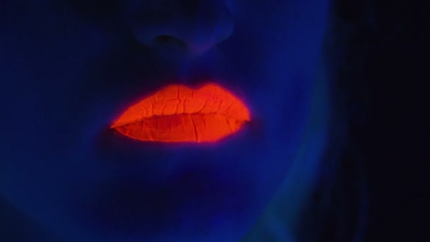 Молодая девушка с красными губами показывает язык в ультрафиолетовом свете — стоковое видео