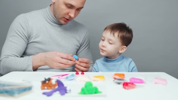 Disparos de padre e hijo haciendo animales de plastilina sobre fondo gris — Vídeos de Stock