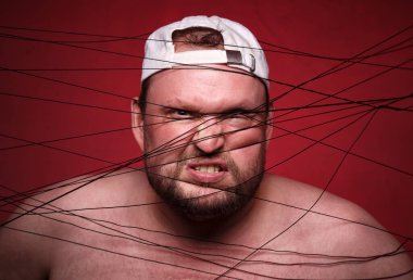 Kırmızı arka planda siyah ipliğe dolanmış şişman adamın fotoğrafı.