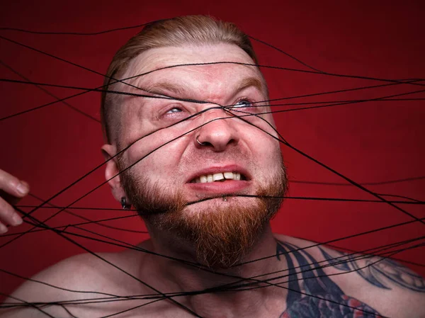 Tangled in black threads bearded man on red background — Stock Photo, Image