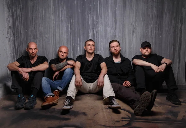 Group of serious tired men sitting on dirty floor — Stock Photo, Image