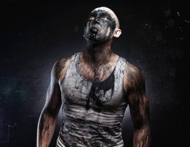 Ağzında siyah çamur olan kel deli adam yukarı bakıyor.