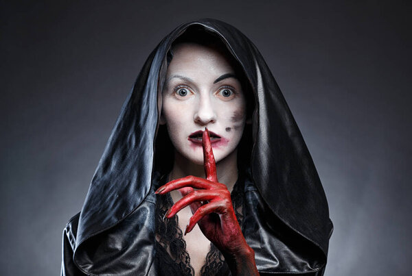 Photo of woman in black leather hood with red hands on black background