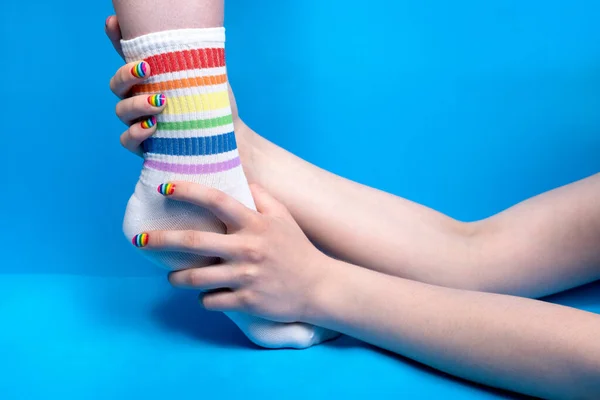 Foto de mãos segurando a perna em meias com cores do arco-íris — Fotografia de Stock