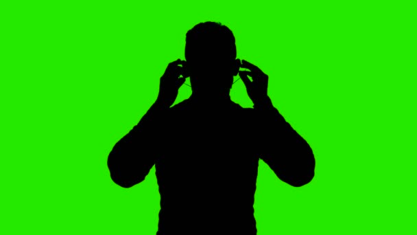 Footage of mans silhouette dressing medical mask on green background — Stock Video