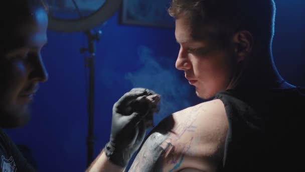 Tattooer får en tatovering på en mandeskulder i en salon – Stock-video