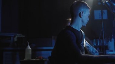 Genç bir adamın omzuna dövme yaptıran bir dövmeciyi vurmak.