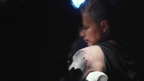 Стрельба в татуировщика, делающего татуировку на плече молодого человека — стоковое видео