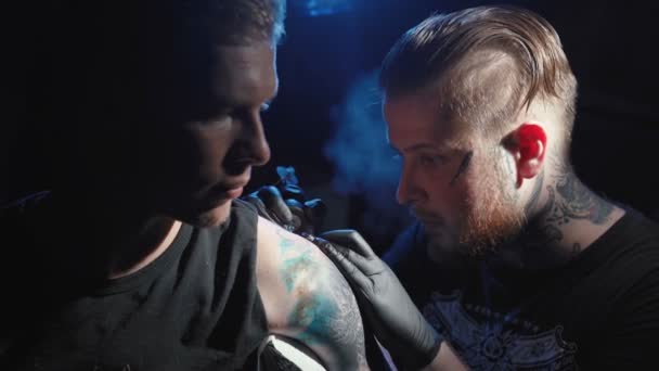 Mistrz robi sobie tatuaż na ramieniu młodego mężczyzny — Wideo stockowe