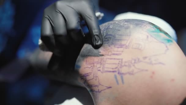 Видео татуировщика, делающего татуировку на плече молодого человека в салоне — стоковое видео