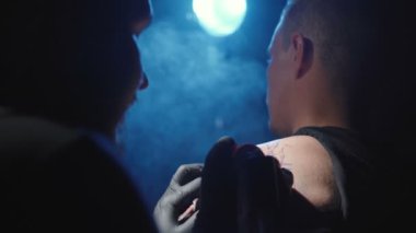 Bir dövmecinin kuaförde bir adamın omzuna dövme yaptırdığı görüntüler.