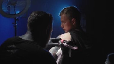 Adamın omzuna dövme yaptıran bir ustanın görüntüsü.