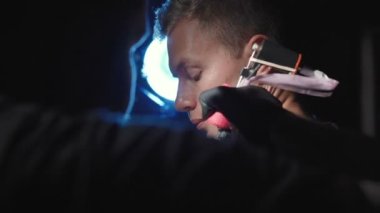 Genç bir adamın omzuna dövme yaptıran usta bir dövmenin çekimi.