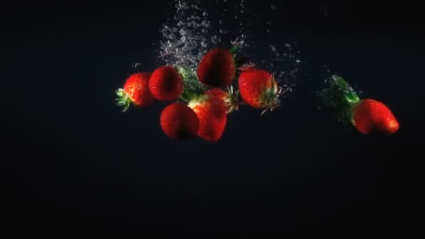 Images de fraises tombantes dans l'eau sur fond noir — Video