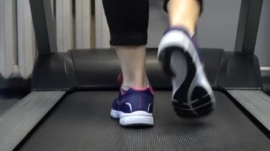 Spor salonunda koşu bandında yürüyen bir kadın görüntüsü.