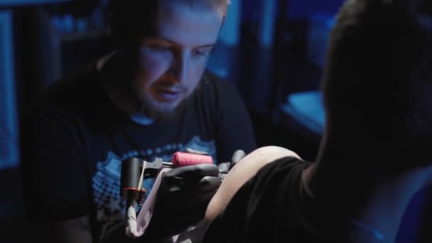 Lövöldözés tetováló művész szerzés egy tetoválás egy fiatal férfi váll egy szalonban — Stock videók