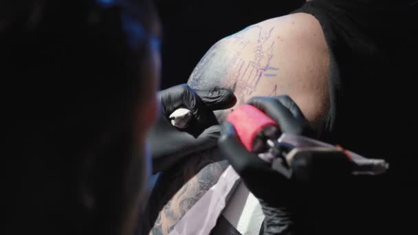 Filmato di un tatuatore che si fa un tatuaggio su una spalla di un giovane uomo in un salone — Video Stock