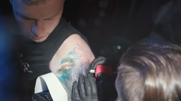 Стрельба мастера, делающего татуировку на плече человека в салоне — стоковое видео