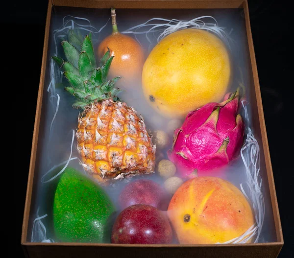 Image de boîte en bois avec des fruits exotiques en fumée sur fond noir — Photo