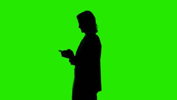 Video van vrouwen silhouet praten op telefoon in pak jas op groene achtergrond — Stockvideo