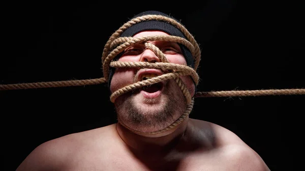 Portrait of binded screaming fat man in cap with rope on face — Stock Photo, Image