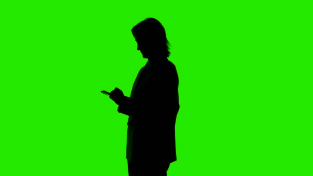 Video van vrouwen silhouet in pak jas met smartphone op groene achtergrond — Stockvideo