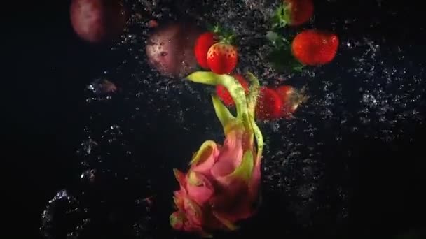 Schießen von fallenden exotischen Früchten im Wasser auf schwarzem Hintergrund — Stockvideo