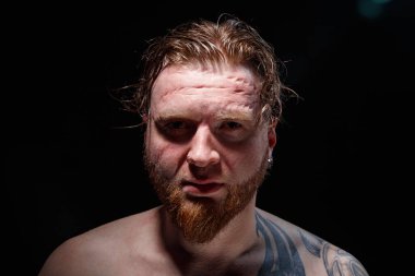 Siyah arka planda kızıl saçlı dövmeli bir adam resmi.